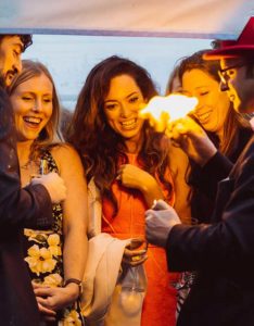 The Magician creates a ball of fire at a partysurrounded by people laughing