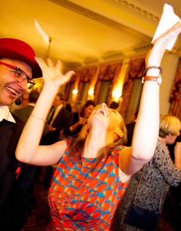 A woman holds up a card while another applauds at a party. The magician is between them.
