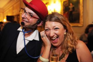 A lady holding a stethoscope to her ear and laughing with the magician at a birthday party