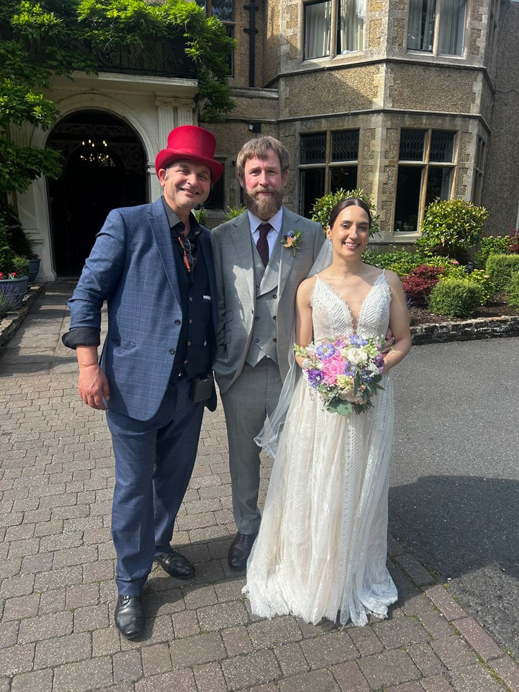 wedding magician Red Hat Magic standing outside Camberley wedding venue the MacDonald Frimley Hall Hotel and Spa, together with the bride and groom.