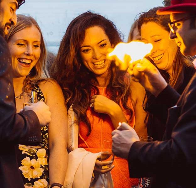 The Magician creates a ball of fire at a partysurrounded by people laughing